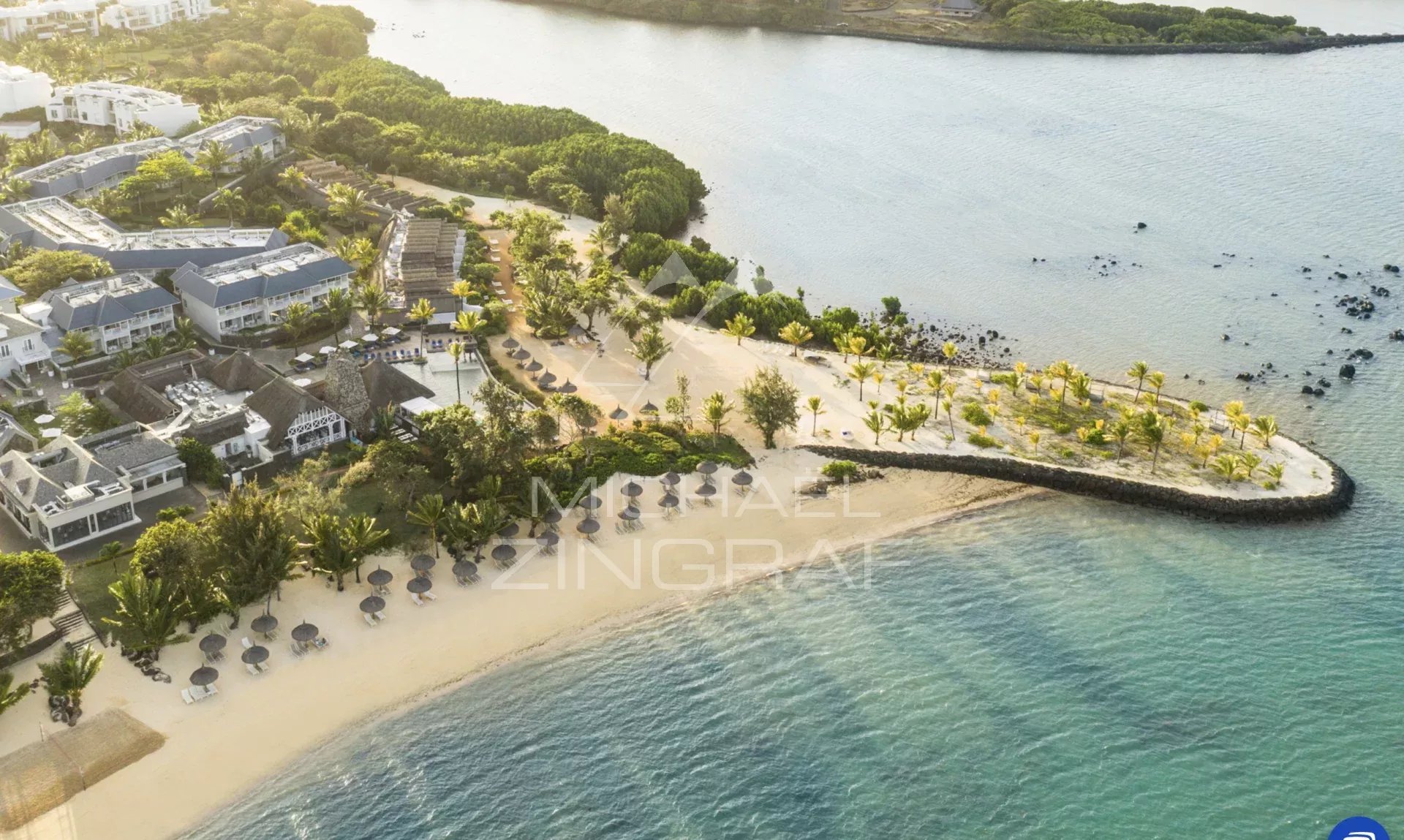 Vue aérienne d'une plage avec des parasols et des palmiers, bordée par un parcours de golf.