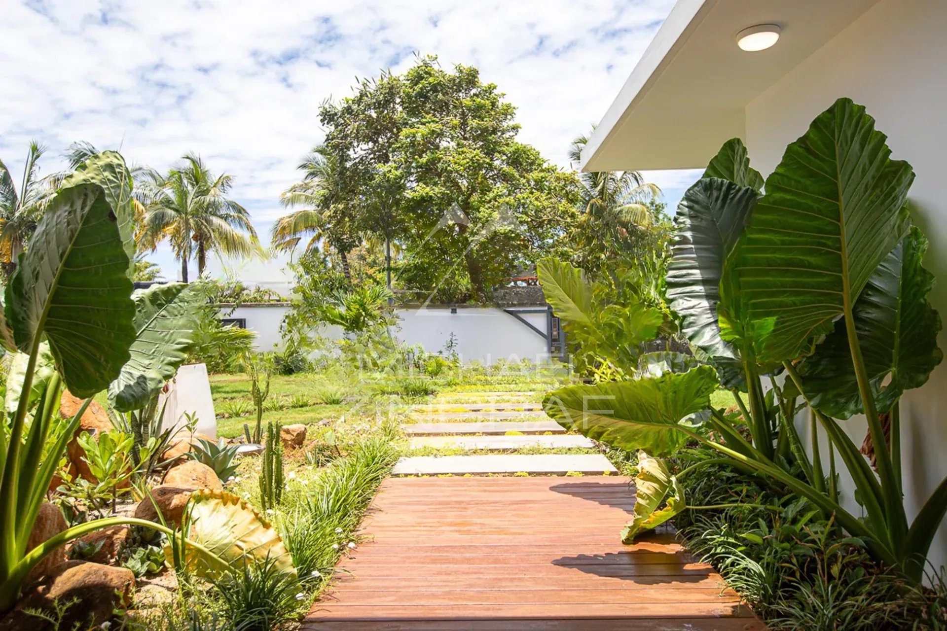 Allée menant à une villa de luxe entourée de verdure et de plantes tropicales.