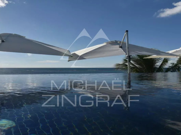 View of the infinity pool with parasols and sea in the background in Pereybere.