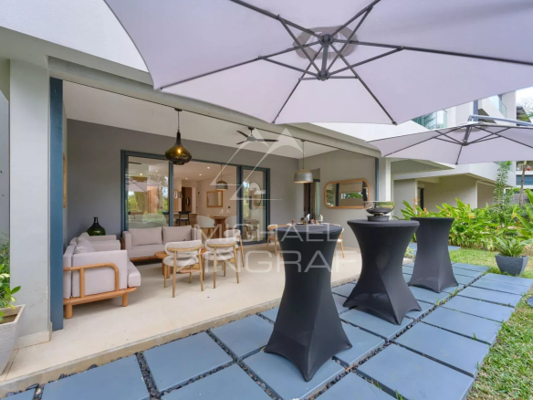 Apartment terrace with modern furniture and parasols, surrounded by greenery.