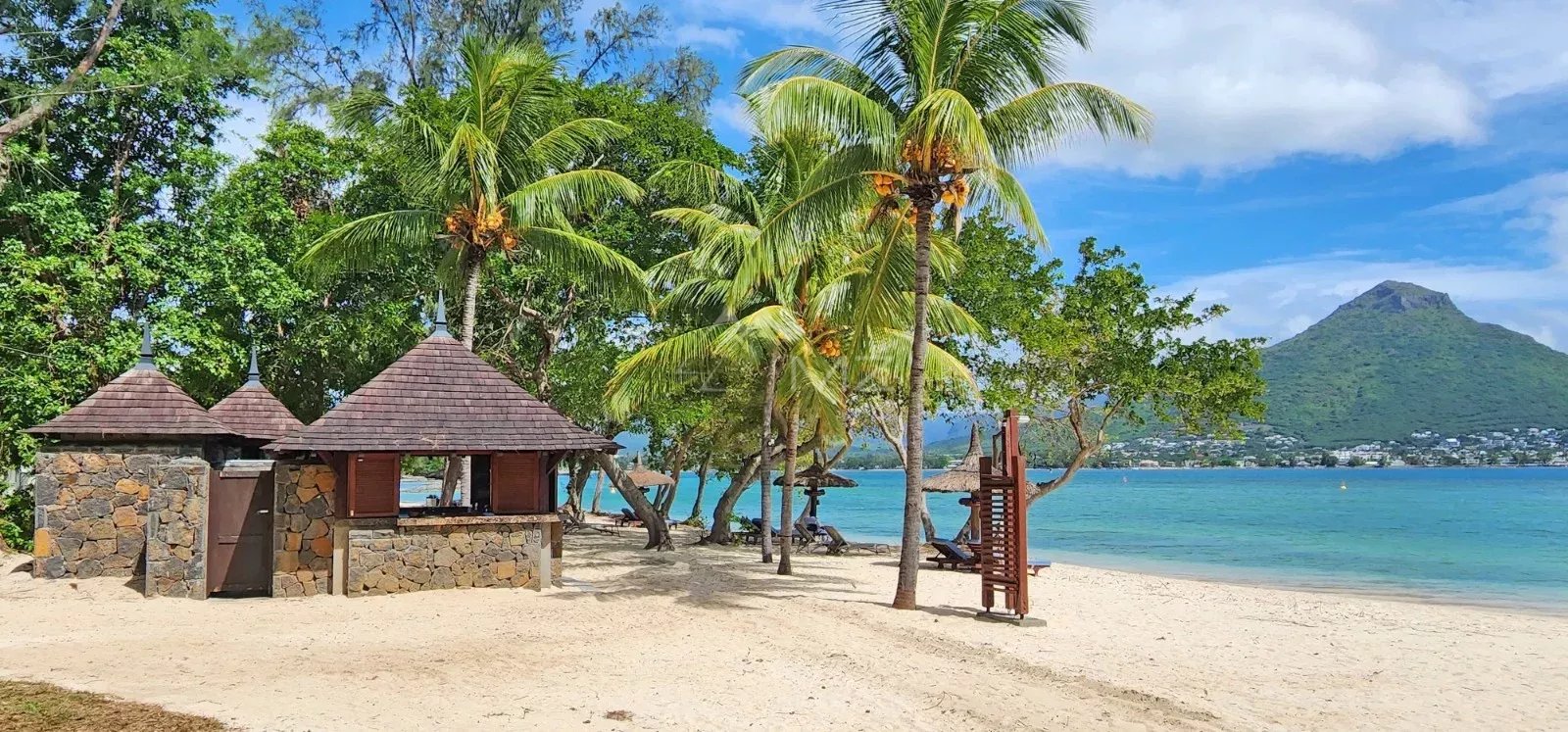 Beach and huts by the water Beach with huts and palm trees, sea view and a mountain in the background.