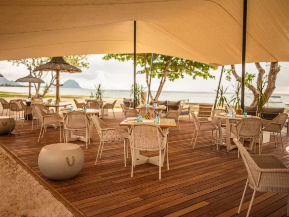 Seaside restaurant terrace with wicker tables and chairs, overlooking the beach and lagoon.
