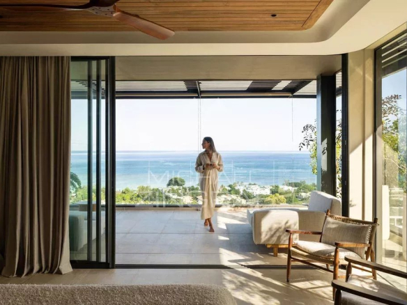Intérieur d'un penthouse avec vue sur l'océan Indien à Rivière Noire, femme en peignoir sur le balcon.
