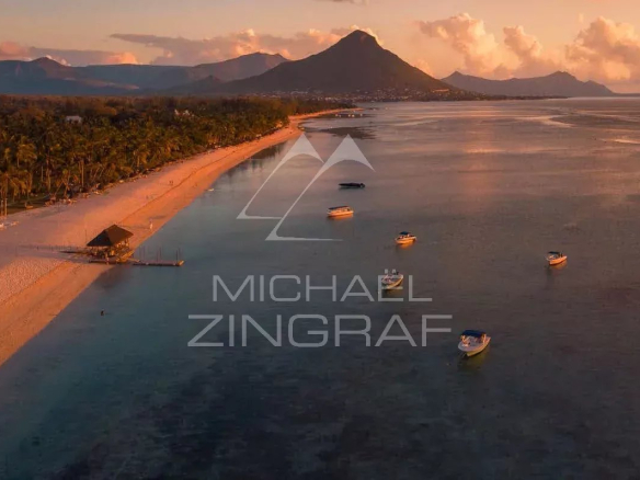 Vue aérienne de la plage et des bateaux à Tamarin, avec des montagnes en arrière-plan au coucher de soleil.
