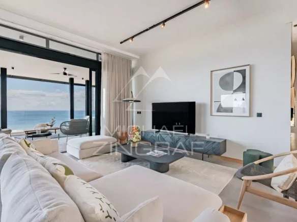 Salon lumineux d'un appartement avec vue sur l'océan, mobilier moderne et terrasse extérieure.