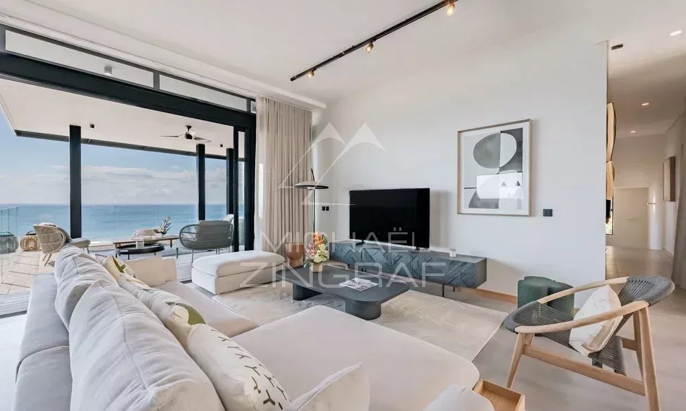 Appartement de 3 Chambres à Rivière Noire Salon lumineux d'un appartement avec vue sur l'océan, mobilier moderne et terrasse extérieure.
