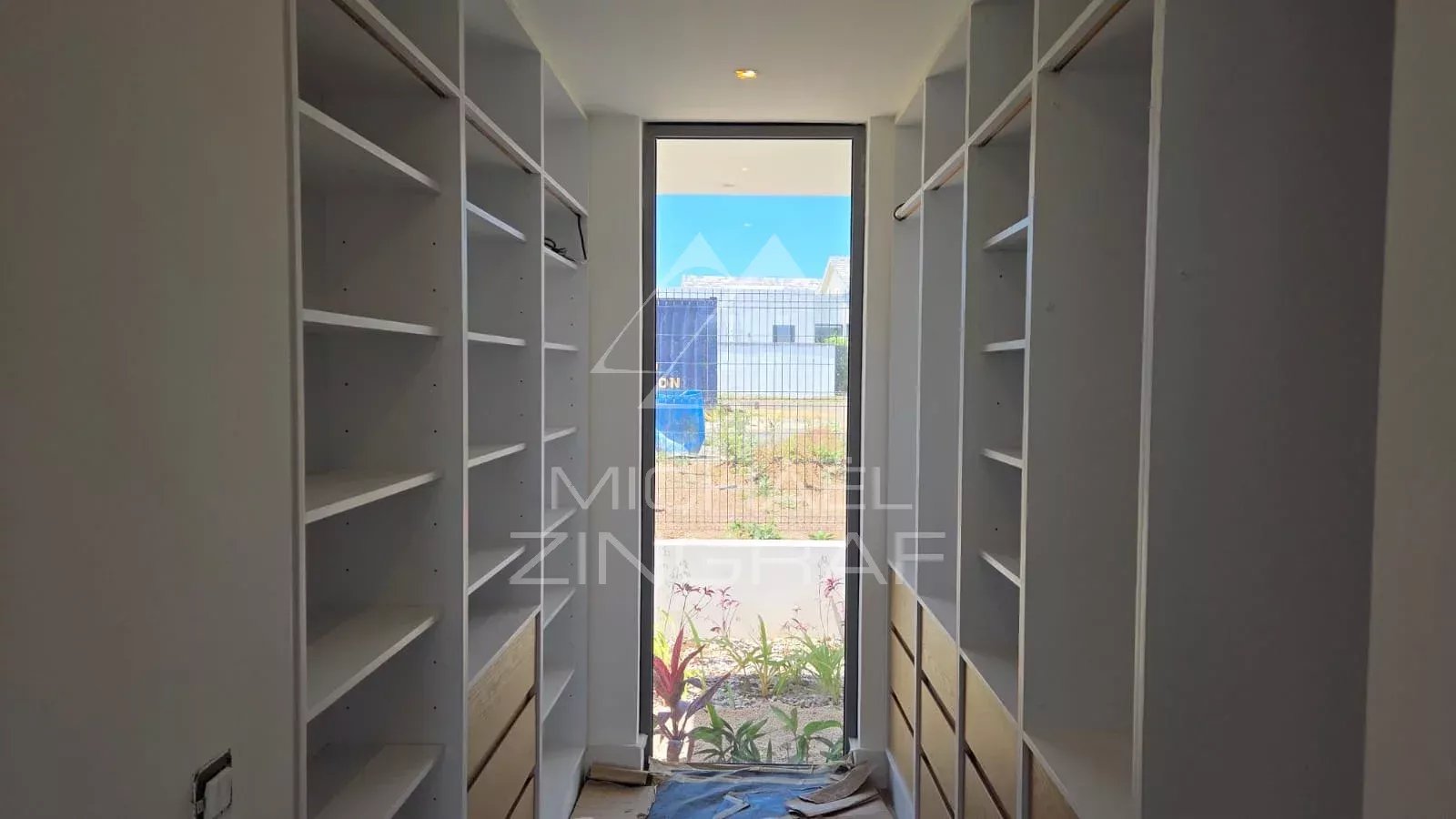 Intérieur d'une villa en construction avec des étagères et une vue sur l'extérieur.