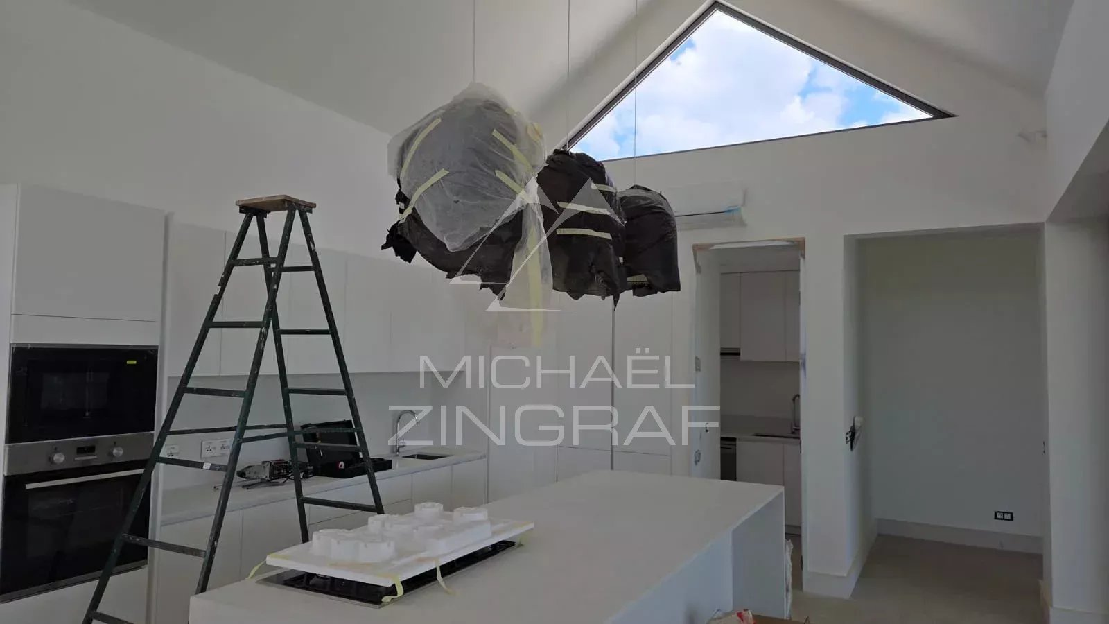 Intérieur d'une villa en construction avec cuisine moderne et éclairage suspendu.