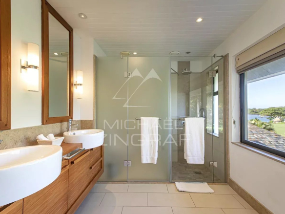 Salle de bain moderne avec deux lavabos et douche en verre, vue sur le lagon
