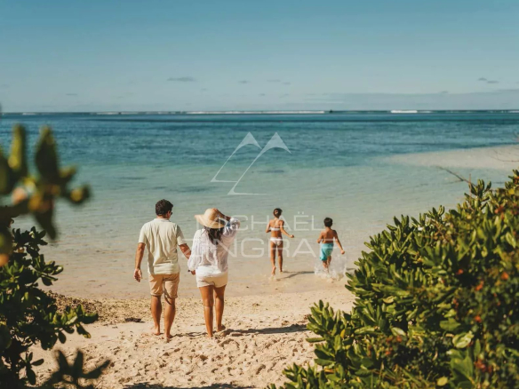 A family walking on the beach near a lagoon at Pointe d'Esny, surrounded by vegetation.