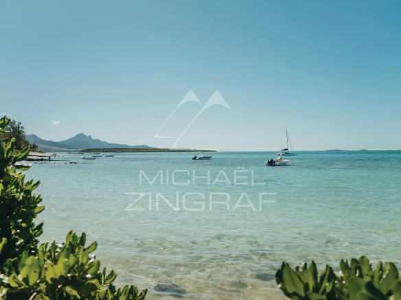 View of a clear lagoon with boats and mountains in the background at Pointe d'Esny.