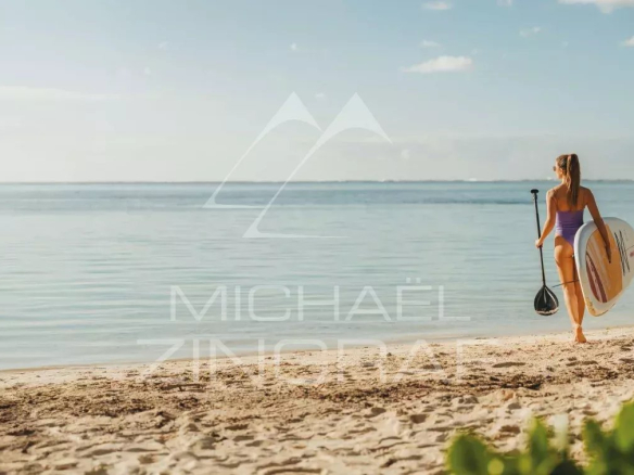 Woman walking on the beach with a paddleboard at Pointe d'Esny, calm lagoon in the background.