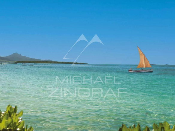 View of a turquoise lagoon with an orange sailboat, surrounded by vegetation.