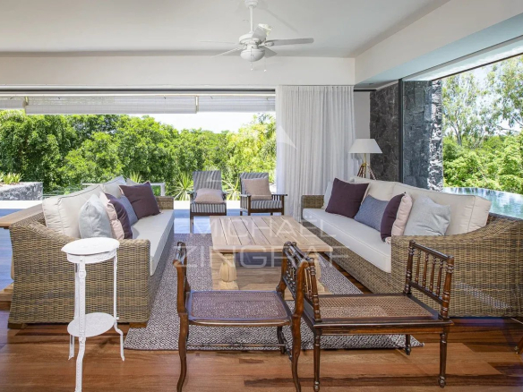 Intérieur d'une villa de prestige avec salon lumineux et mobilier en rotin, vue sur la nature.