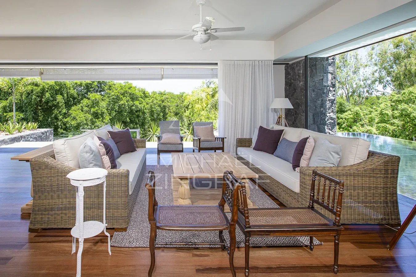 Salon d’une villa de prestige à Haute Rive Intérieur d'une villa de prestige avec salon lumineux et mobilier en rotin, vue sur la nature.