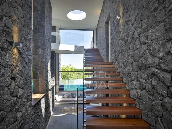 Intérieur d'une villa moderne avec escaliers en bois et murs en pierre à Haute Rive.