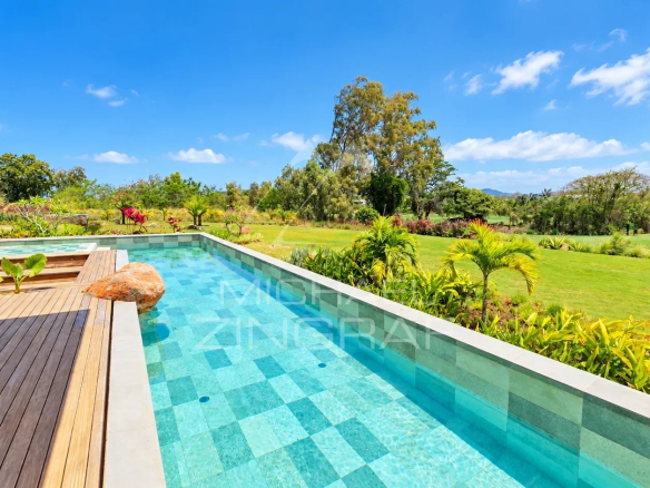 View from the private pool of a contemporary villa with garden and golf course in the background in Beau Champ.
