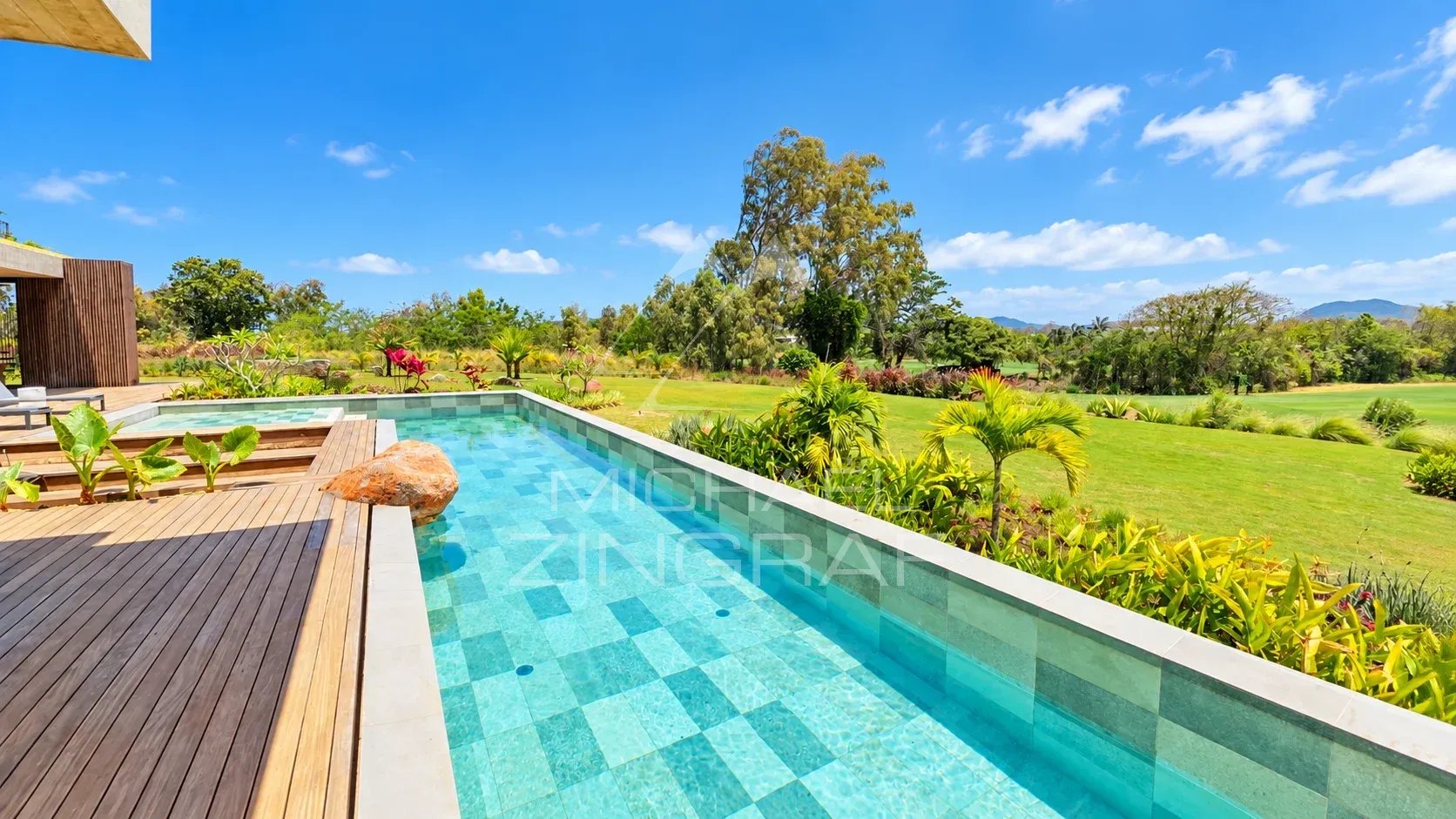 View from the private pool of a contemporary villa with garden and golf course in the background in Beau Champ.