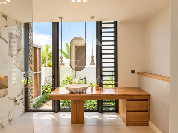 Modern bathroom with wooden sink and large windows overlooking a garden.