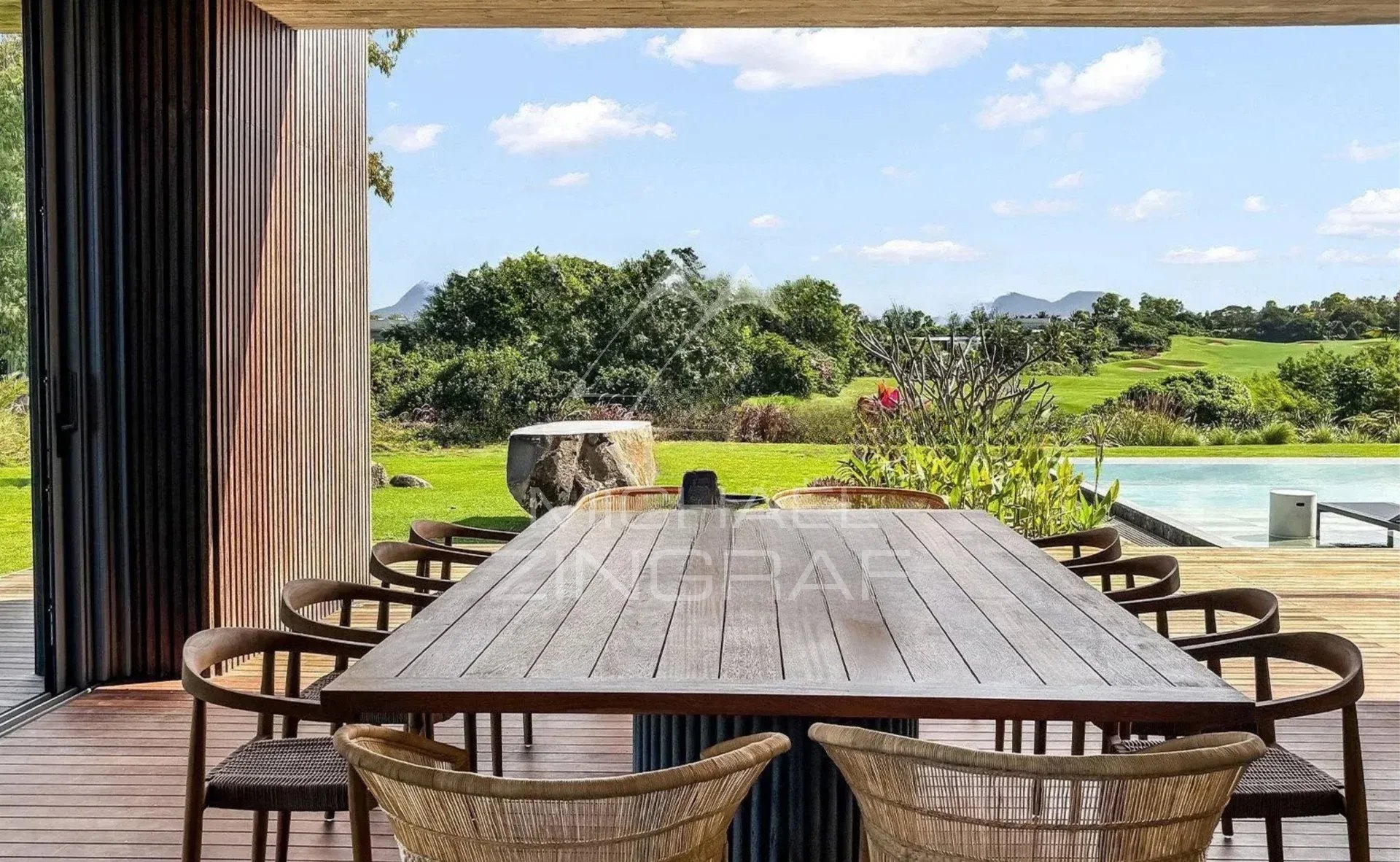 Terrace of a modern villa with a large dining table and views of the golf course and swimming pool.