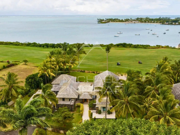 Vue aérienne d'une villa mauricienne avec piscine, golf et lagon turquoise en arrière-plan.