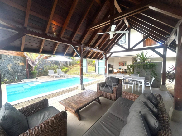 Terrasse couverte avec mobilier et piscine dans un resort à Rivière Noire, près de la plage.