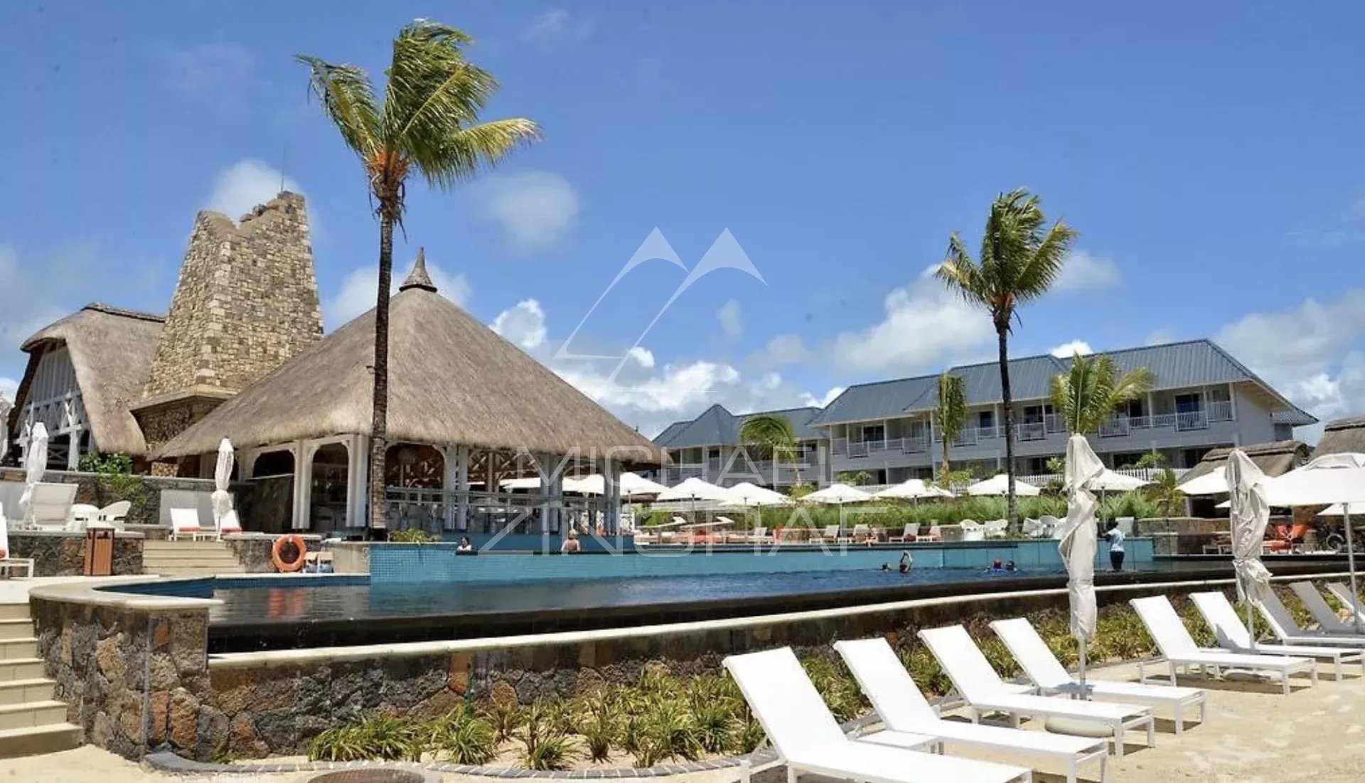 Vue d'un complexe résidentiel avec piscine et palmiers, situé à Azuri Golf and Beach Resort à Haute Rive.