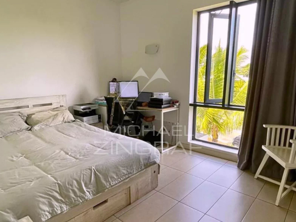 Chambre d'un penthouse avec lit, bureau et fenêtre donnant sur des palmiers.