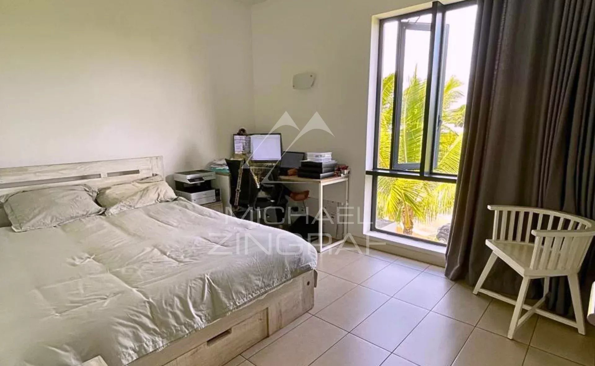 Chambre d'un penthouse avec lit, bureau et fenêtre donnant sur des palmiers.