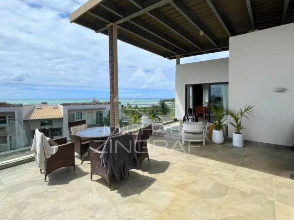 Terrasse d'un penthouse avec vue sur la mer à Haute Rive, mobilier de jardin et ciel nuageux.