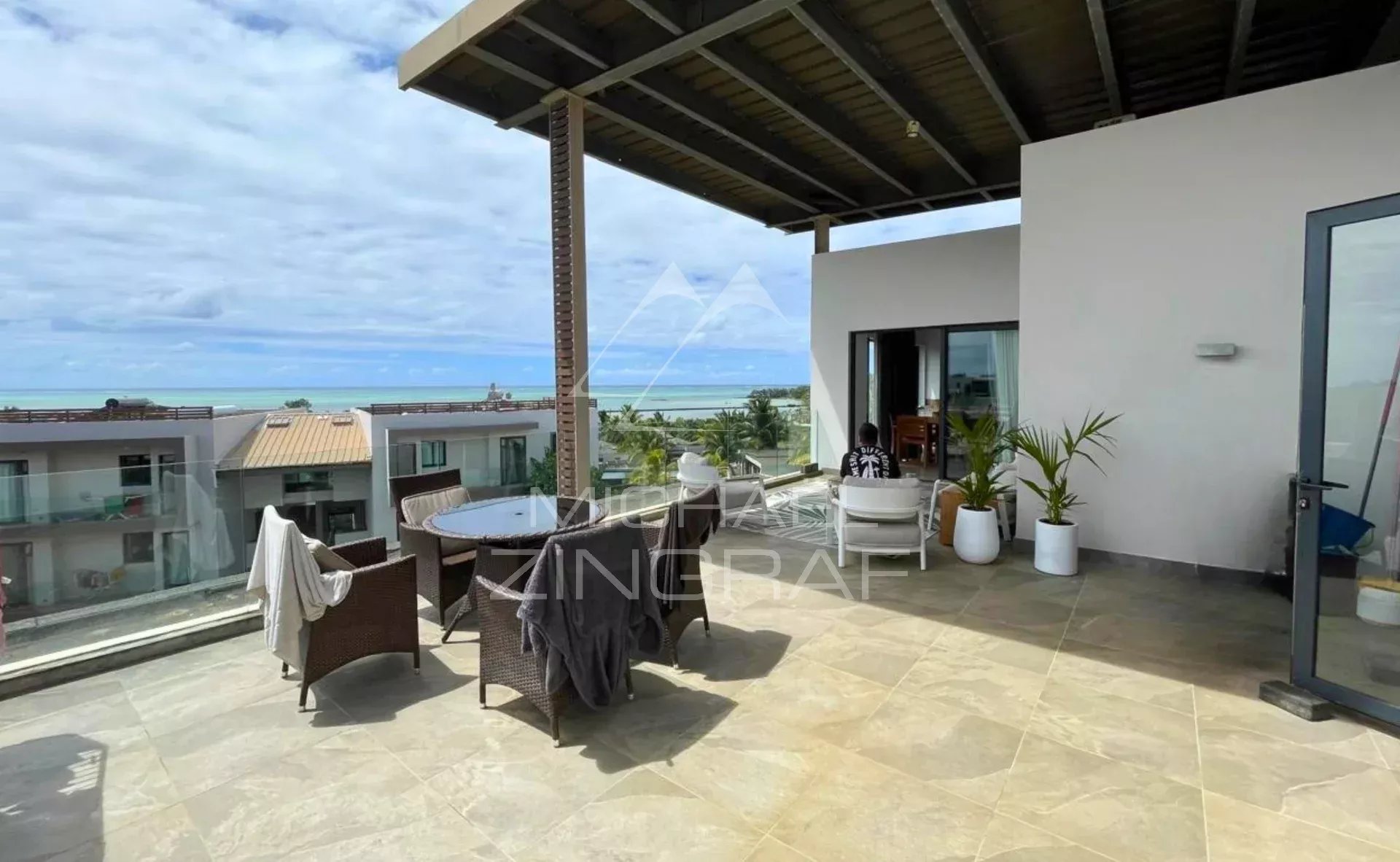 Terrasse d'un penthouse avec vue sur la mer à Haute Rive, mobilier de jardin et ciel nuageux.