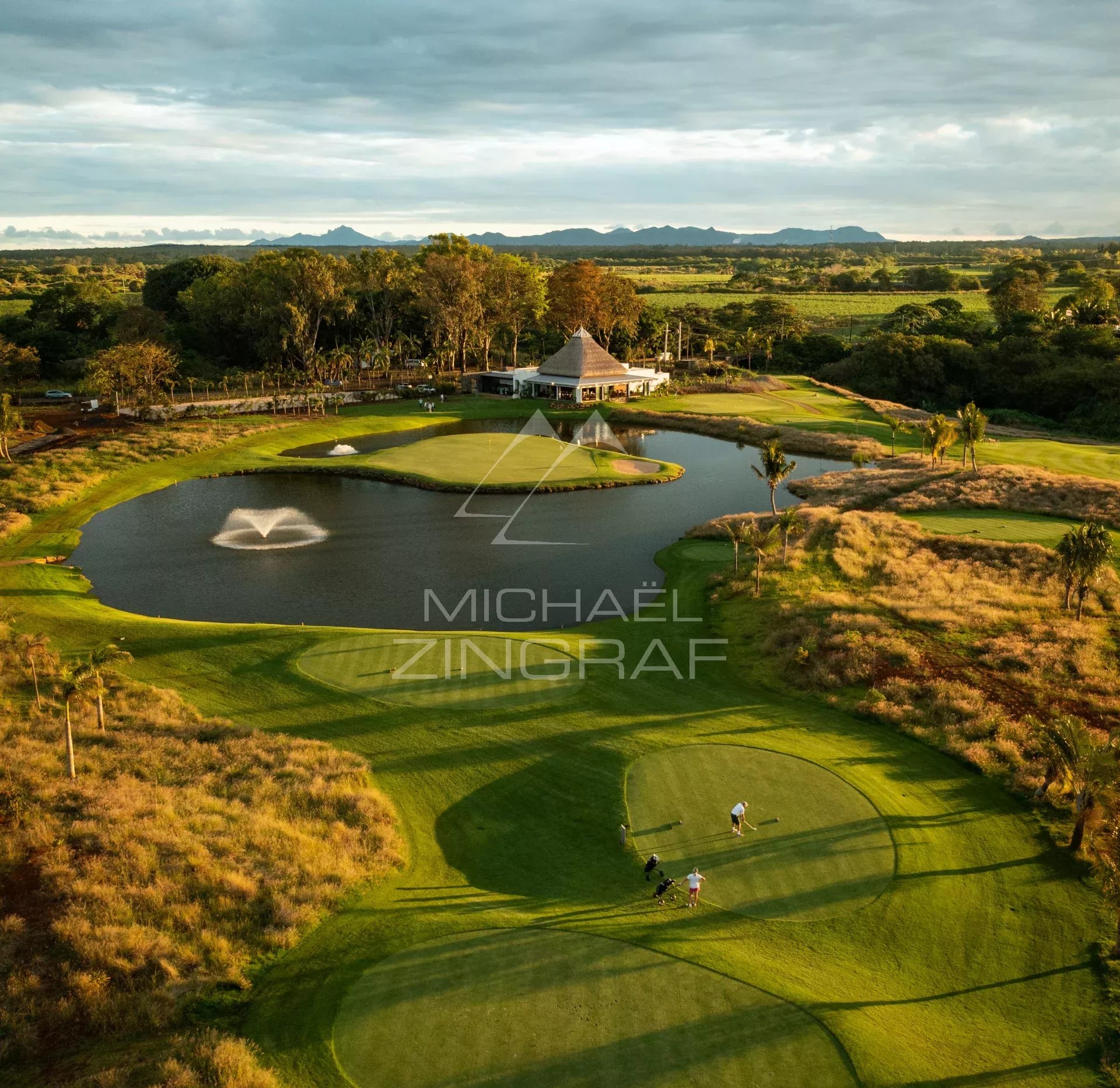 Vue aérienne d'un parcours de golf avec un lac et des joueurs sur le green.
