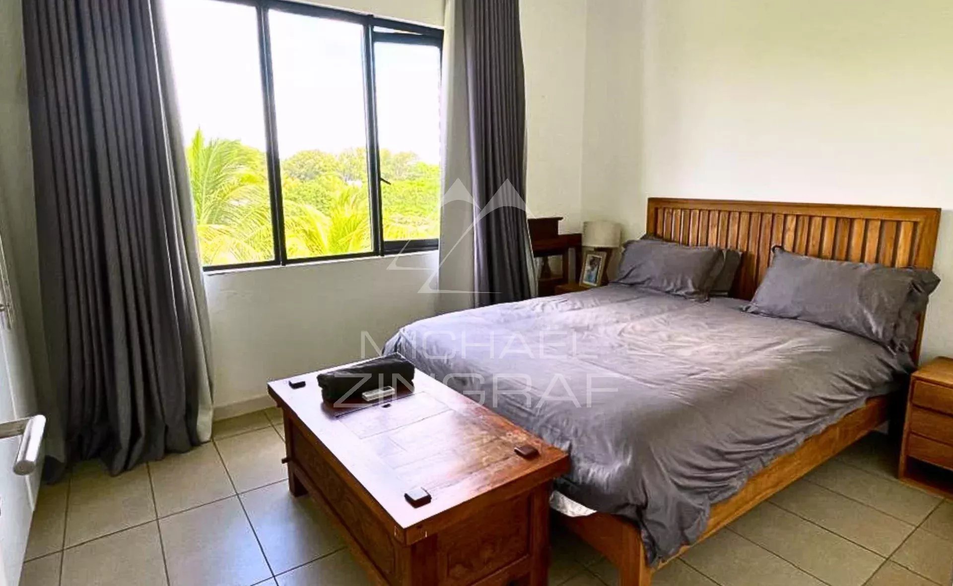 Chambre d'un penthouse avec lit double et fenêtre donnant sur un paysage verdoyant.