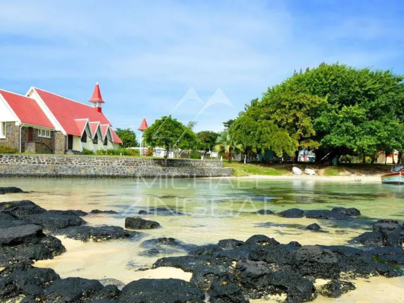 Vue d'une église avec un toit rouge et des arbres au bord d'une plage à Anse La Raie, Île Maurice.