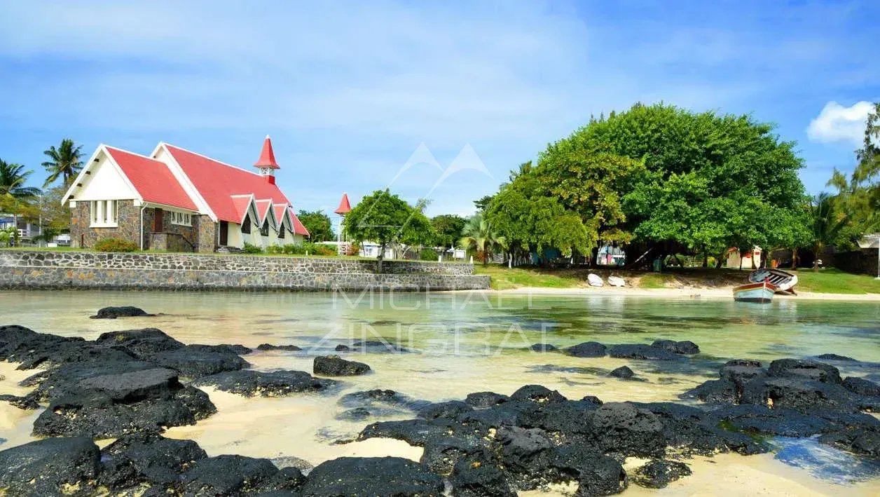 Vue d'une église avec un toit rouge et des arbres au bord d'une plage à Anse La Raie, Île Maurice.