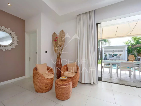 Intérieur d'une villa contemporaine avec des fauteuils en rotin et une vue sur la piscine extérieure.