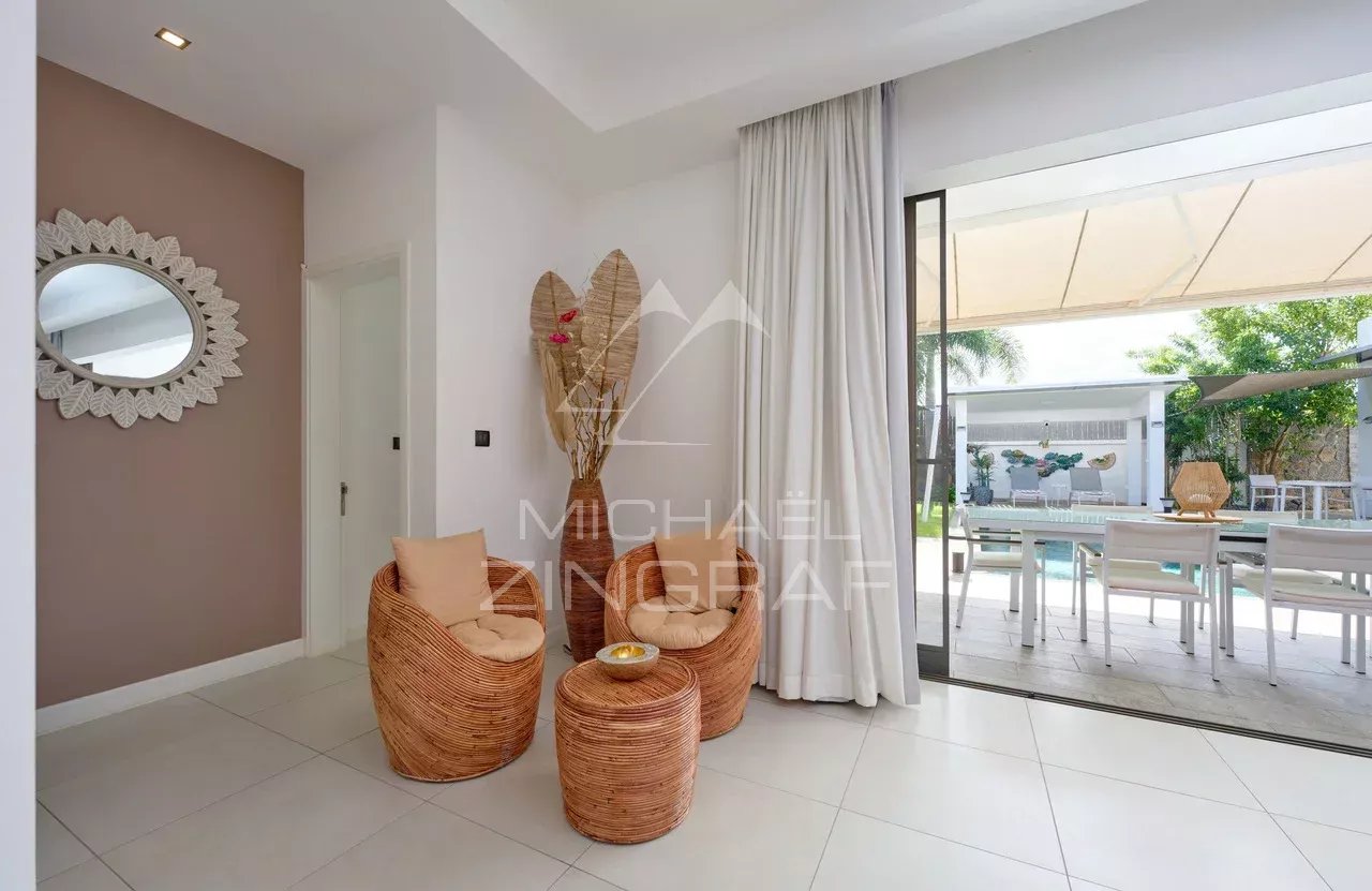 Intérieur d'une villa contemporaine avec des fauteuils en rotin et une vue sur la piscine extérieure.