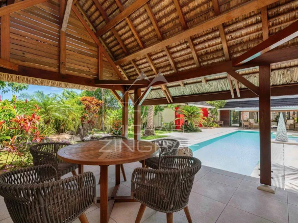 Terrasse en bois avec table et chaises, piscine et jardin luxuriant en arrière-plan.
