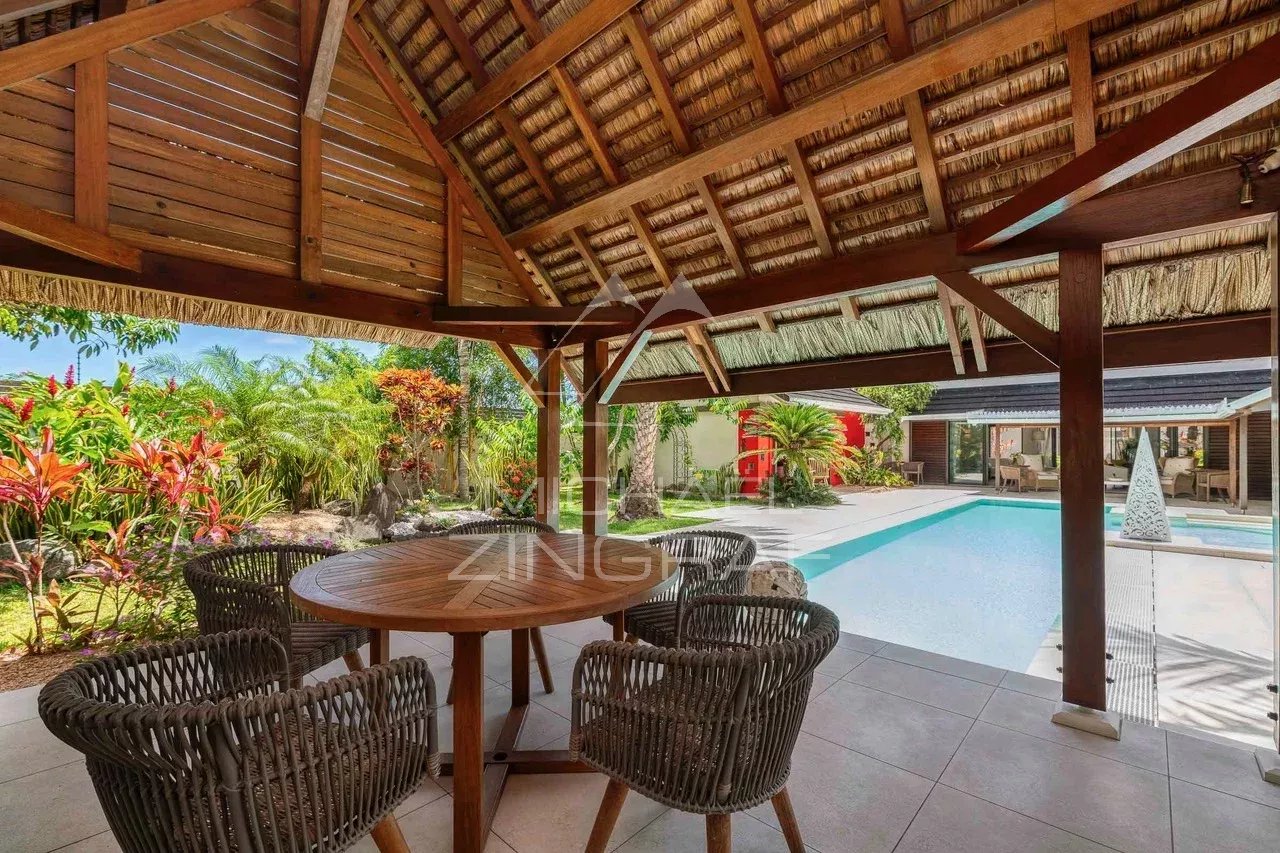 Terrasse en bois avec table et chaises, piscine et jardin luxuriant en arrière-plan.