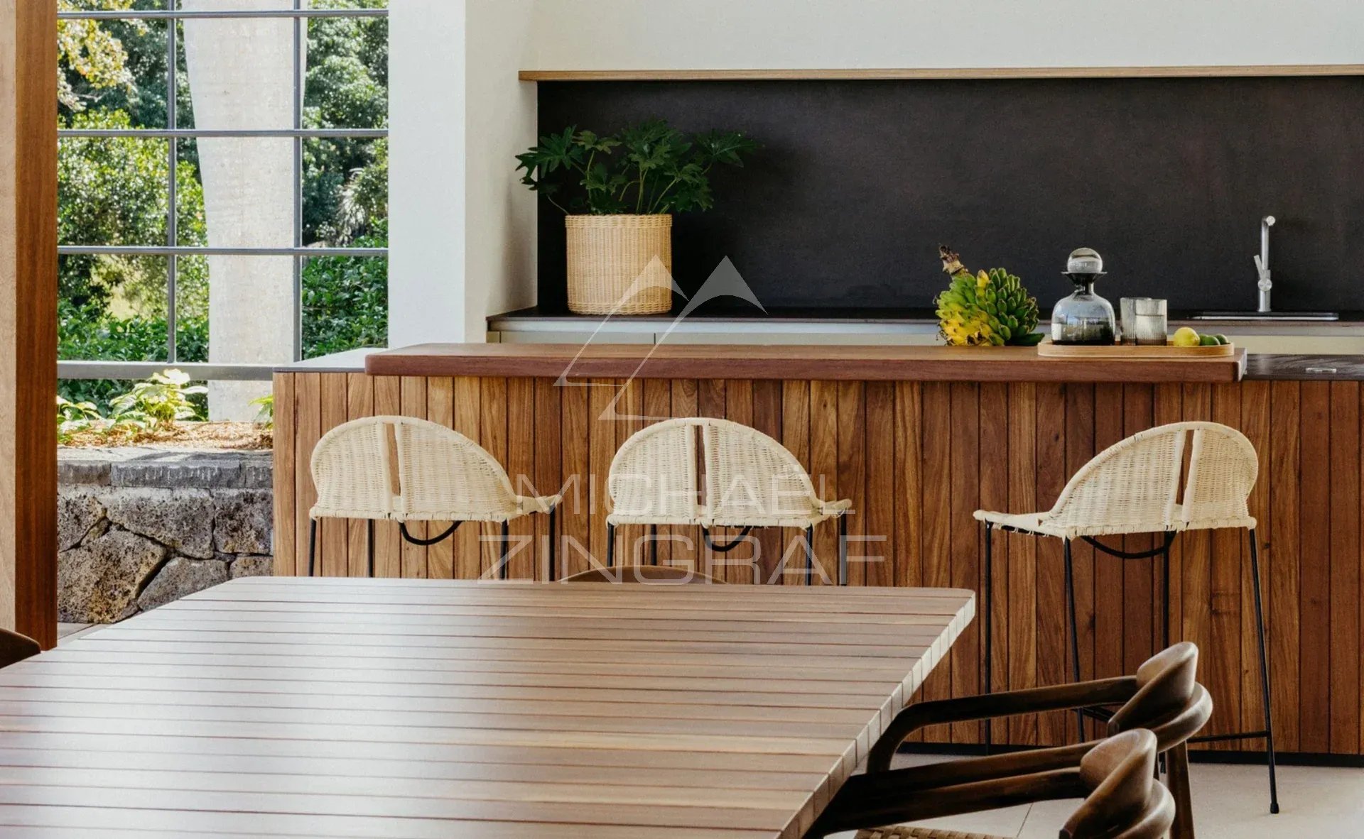Intérieur de la Villa Vacoas à Bel Ombre Intérieur moderne d'une villa avec cuisine en bois et chaises en osier, entouré de verdure.