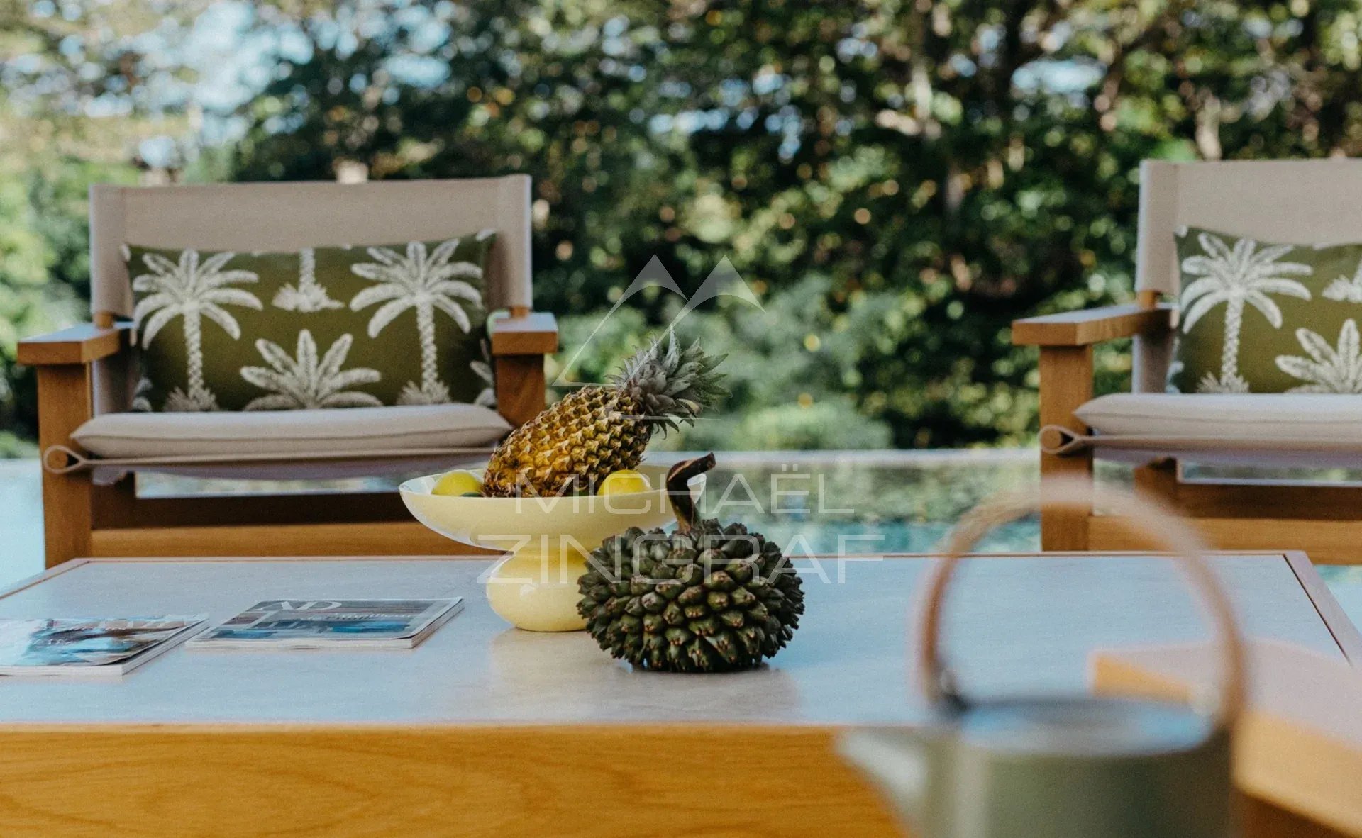 Détails de la Villa Vacoas Table basse avec des ananas et des magazines, chaises en bois en arrière-plan, nature environnante