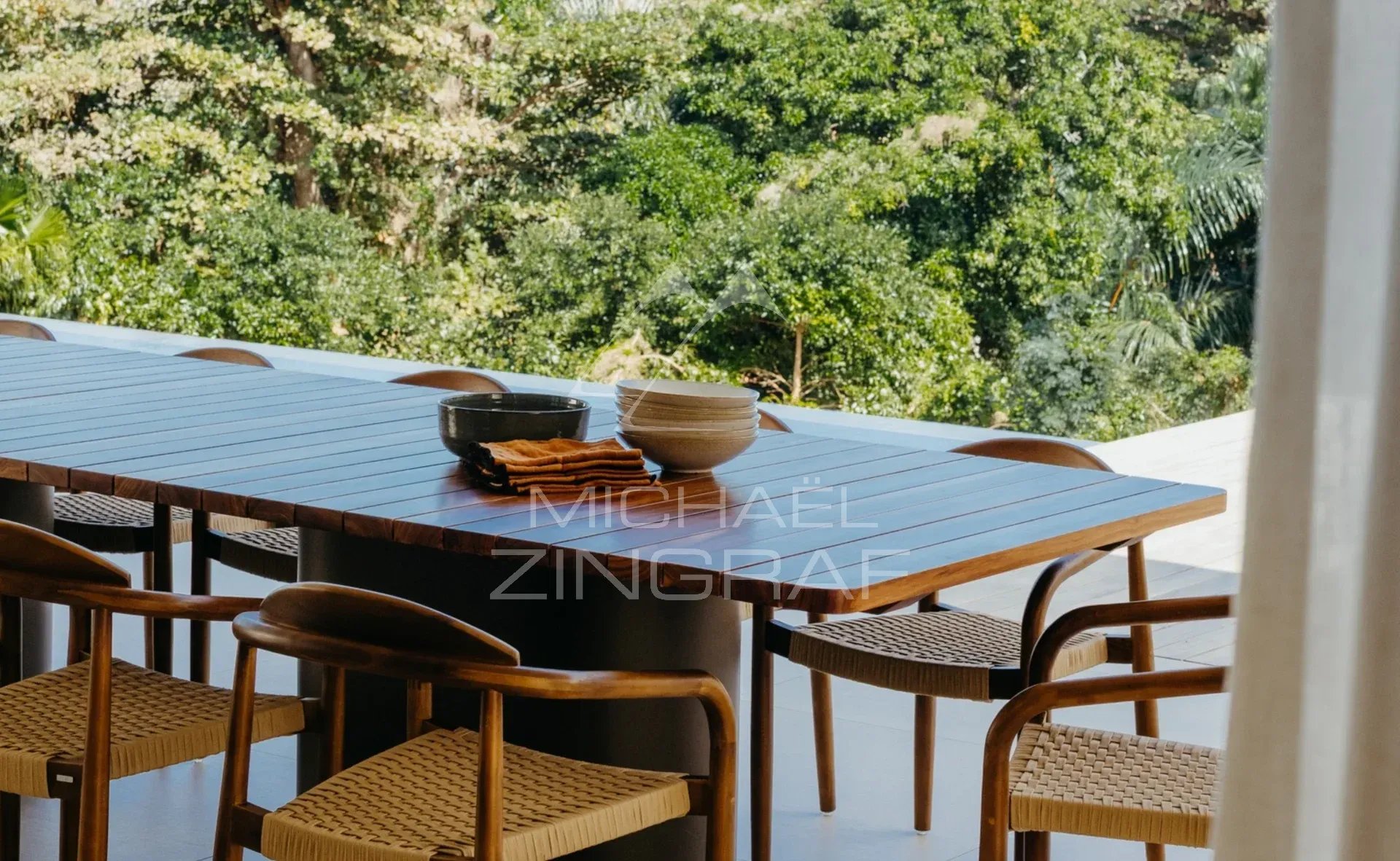 Terrasse de la Villa Vacoas Table en bois avec chaises en rotin sur une terrasse avec vue sur la nature verdoyante.