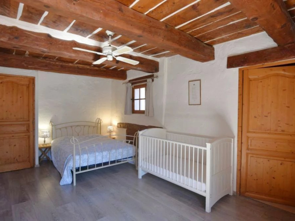 Rustic bedroom with exposed wooden beams, queen bed, white crib, two nightstands, and ceiling fan.