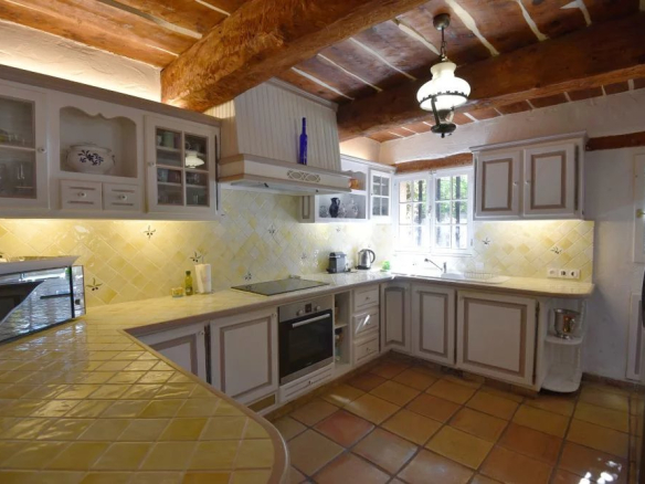 Cozy rustic kitchen with exposed wooden beams, yellow tiled counters, and white cabinets under warm lighting