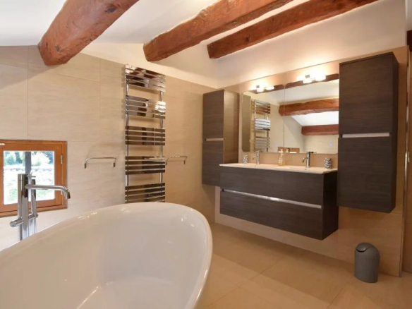 Modern bathroom with a freestanding white tub, double sink vanity, and exposed wooden ceiling beams.