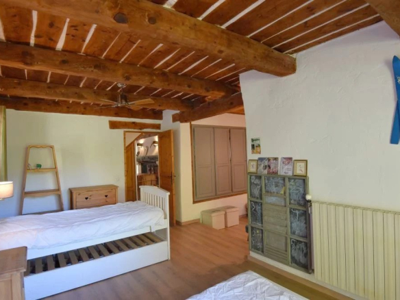 Bedroom with exposed wooden beam ceiling, a white single bed, ladder shelf, and dresser; blue skis mounted on the wall.