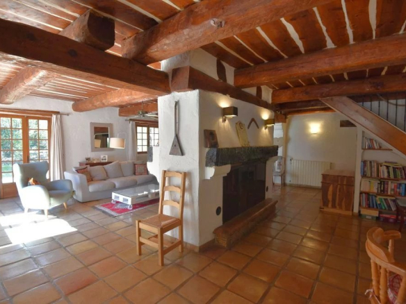 Cozy rustic living room with exposed wooden beams, a stone fireplace, and a seating area with sofa, chairs, and coffee table.