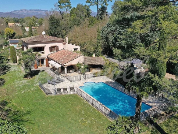 A Mediterranean-style house with tiled roof and a bright blue rectangular pool in a fenced yard, surrounded by trees and hills.