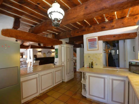 Rustic kitchen with exposed timber beams, white cabinets, and tiled countertops around a central island.