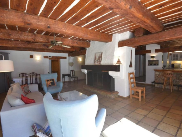 Rustic living room with exposed wooden beams, white plaster walls, and a large stone fireplace with a dark mantle.
